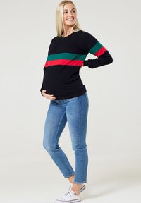 Schwarzer Langarm-Sweatshirt mit grünen und roten horizontalen Streifen, kombiniert mit blauen Skinny-Jeans und weißen Sneakern.