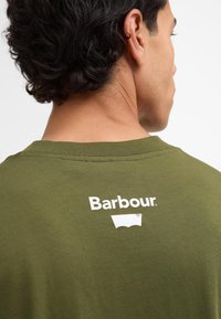 T-shirt en coton vert olive avec un logo "Barbour" blanc sur le haut du dos. Texture lisse et design classique à col rond.