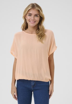 Haut à manches courtes, ample, en tissu pêche doux avec un col rond et une texture subtile. Associé à un jean bleu foncé.