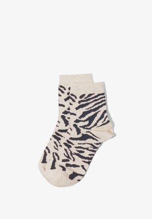 Beige Knöchelsocken mit auffälligem schwarzem Zebramuster, flach auf weißem Hintergrund ausgebreitet.