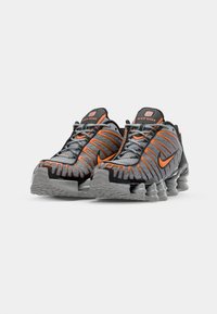 Nike Shox shoes feature a grey mesh upper with orange accents, unique patterned sole, and cushioned heel for support.