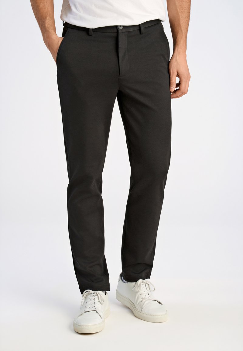 Pantaloni neri realizzati in tessuto leggero, fit su misura, con design a davanti piatto e tasche laterali, abbinati a sneakers bianche.