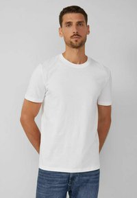 Camiseta blanca de algodón de manga corta, con diseño de cuello redondo, textura suave y corte básico. Se lleva con jeans azules.