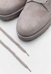 Chaussures en suède gris avec une surface texturée, bout rond et lacets gris placés à côté. La semelle est à motif pour une meilleure adhérence.