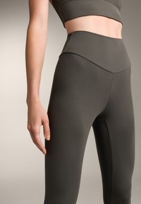 Vysoké legíny v tmavě olivově zelené barvě, které mají hladkou, elastickou látku s přiléhavým střihem a jemným švem.