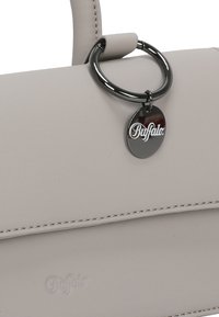 Bolso de mano gris claro hecho de cuero suave, con un anillo circular y una etiqueta de metal con el logo "Buffalo". Detalle de costura visible.