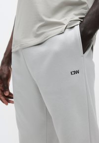 Αθλητικό σορτς ανοιχτού γκρι χρώματος με ομαλή υφή, διακοσμημένο με μαύρο λογότυπο και πλαϊνές τσέπες, συνδυασμένο με ανοιχτό γκρι τοπ από δίχτυ.