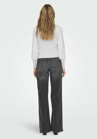 Graue weite Jeans mit hoher Taille, fünf Taschen und einem weichen Denimstoff. Kombiniert mit einem enganliegenden weißen Langarmoberteil.
