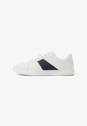 Zapatillas de cuero blancas con un panel diagonal azul marino, puntera redonda y cierre de seis ojales. Textura suave y diseño de perfil bajo.