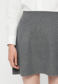 Grå ullskjørt med en utvidet design, glatt tekstur og sømmet kant. Kombinert med en hvit button-up skjorte.