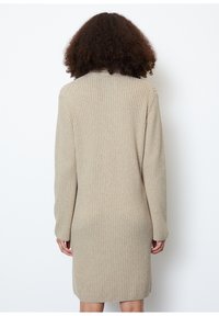 Robe en maille côtelée beige avec manches longues, encolure ronde et coupe décontractée, s'étendant jusqu'au milieu des cuisses. Présente un motif texturé subtil.