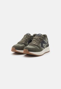 Zapatillas deportivas en verde oliva con acentos negros, de ante texturizado y con una media suela blanca. Cuentan con cierre de cordones y una suela de goma.