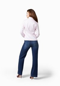 Camicia aderente rosa chiaro con colletto alto, abbinata a jeans a gamba larga blu scuro e tacchi alti marroni, vista da dietro.