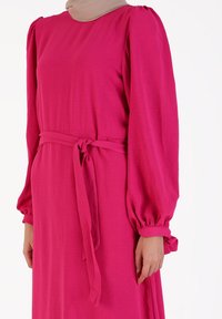 Long-sleeved, pink dress made of lightweight fabric. Features a belted waist and gathered sleeves. Soft texture with a smooth finish.
