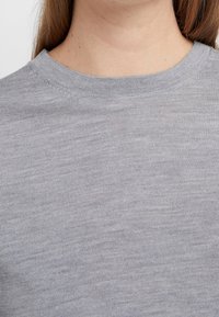 Šedý, lehký svetr s kulatým výstřihem v žebrované textuře. Hladký povrch s jemnými variacemi v látce.