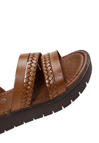 Sandalo in pelle marrone con cinturini intrecciati, soletta imbottita e suola nera testurizzata. Presenta un profilo basso e un design minimalista.