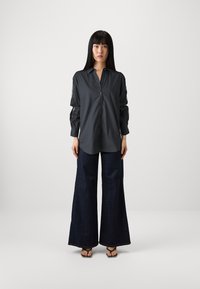 Long-sleeve dark gray shirt with a button-down front and sheer paneling on sleeves, paired with wide-leg dark denim trousers and black sandals.