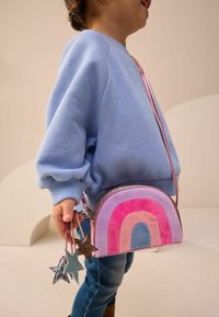 Okrągła torebka na ramię z tęczowym wzorem w pastelowych kolorach. Posiada różowy pasek i błyszczące akcenty w kształcie gwiazdek. Miękka tekstura.