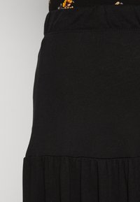 Närbild av svart tygkjol med sammanknuten sömdetalj vid nederkanten, bärs tillsammans med en blommönstrad topp.