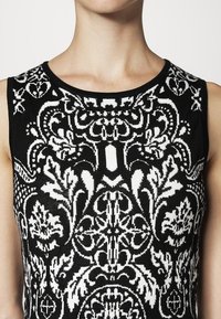 Top senza maniche bianco e nero con intricati motivi floreali e geometrici, con scollatura rotonda e tessuto a maglia testurizzato.