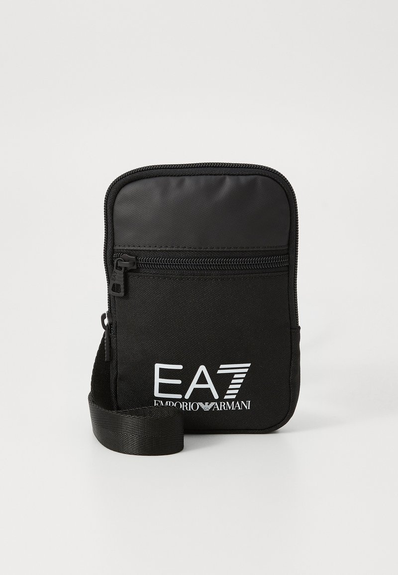 Melnā neilona mazā soma ar rāvējslēdzēju, priekšpusē ar drukātu balto logo "EA7 Emporio Armani" un regulējamu siksniņu.