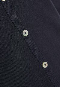 Jūras zila kardigāna adījums no smalkas auduma, kas iezīmē v-veida kakla izgriezumu, ribotu apdari un gaismas krāsas pogas ar apaļu dizainu un centrālajām atverēm.