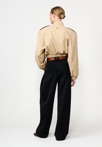 Kohvatu cropped jakk puffsete varrukatega ja elastse äärega, millele on sobitatud kõrge vöökoha mustad püksid. Vööl on pruun vöödetail.