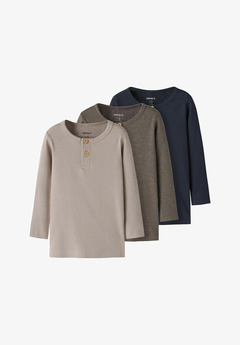 Trois chemises henley à manches longues en maille côtelée pour enfants en beige, marron et marine, chacune avec deux boutons en bois au niveau du col.