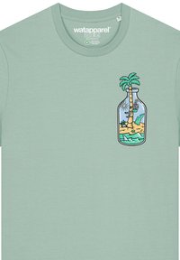 T-shirt vert menthe en tissu doux, avec un design imprimé d'une bouteille contenant des palmiers et des éléments de plage sur le côté gauche de la poitrine.