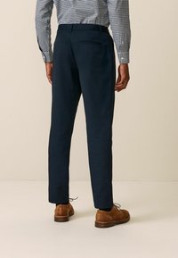Marineblaue, taillierte Hose mit geradem Schnitt, weicher Textur und einer einzelnen Gesäßtasche, kombiniert mit braunen Wildlederschuhen.