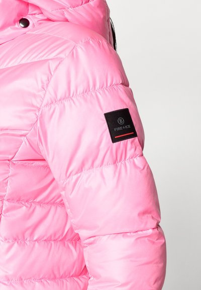 Ροζ φουσκωτό jacket με γυαλιστερή υφή, που διαθέτει ένα μαύρο λογότυπο πάνω στο μανίκι. Ο σχεδιασμός περιλαμβάνει έλασης τμήματα για μόνωση.