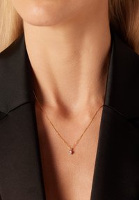 Collier en pendentif en or avec une petite gemme transparente, reposant sur une clavicule nue, associé à un haut noir à col.