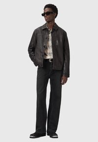 Veste en cuir noir, chemise à carreaux, jean noir et lunettes de soleil noires. La tenue présente un design élégant, des contrastes de texture et des éléments de détail subtils.