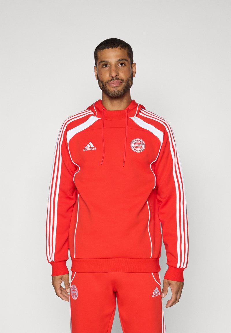 Rød sweatshirt med hvide detaljer, der har hætte, lange ærmer og sidelister. Inkluderer Adidas-logo og emblem fra FC Bayern München.