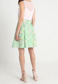 Jupe fleurie verte avec taille ajustée, design plissé et tissu léger. Portée avec un haut sans manches rose clair et des talons à brides.