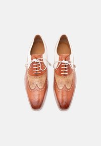 Ζευγάρι δερμάτινων παπουτσιών τύπου brogue σε διχρωμία καφέ με λευκά κορδόνια, φωτογραφημένα από πάνω σε ανοιχτό φόντο.
