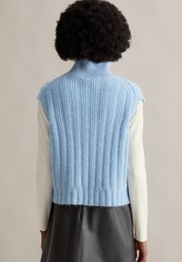 Hellblauer gestrickter Pullover mit hohem Kragen, vertikalen Rippen und cropped Design. Strukturiertes Material und rohe Kanten.