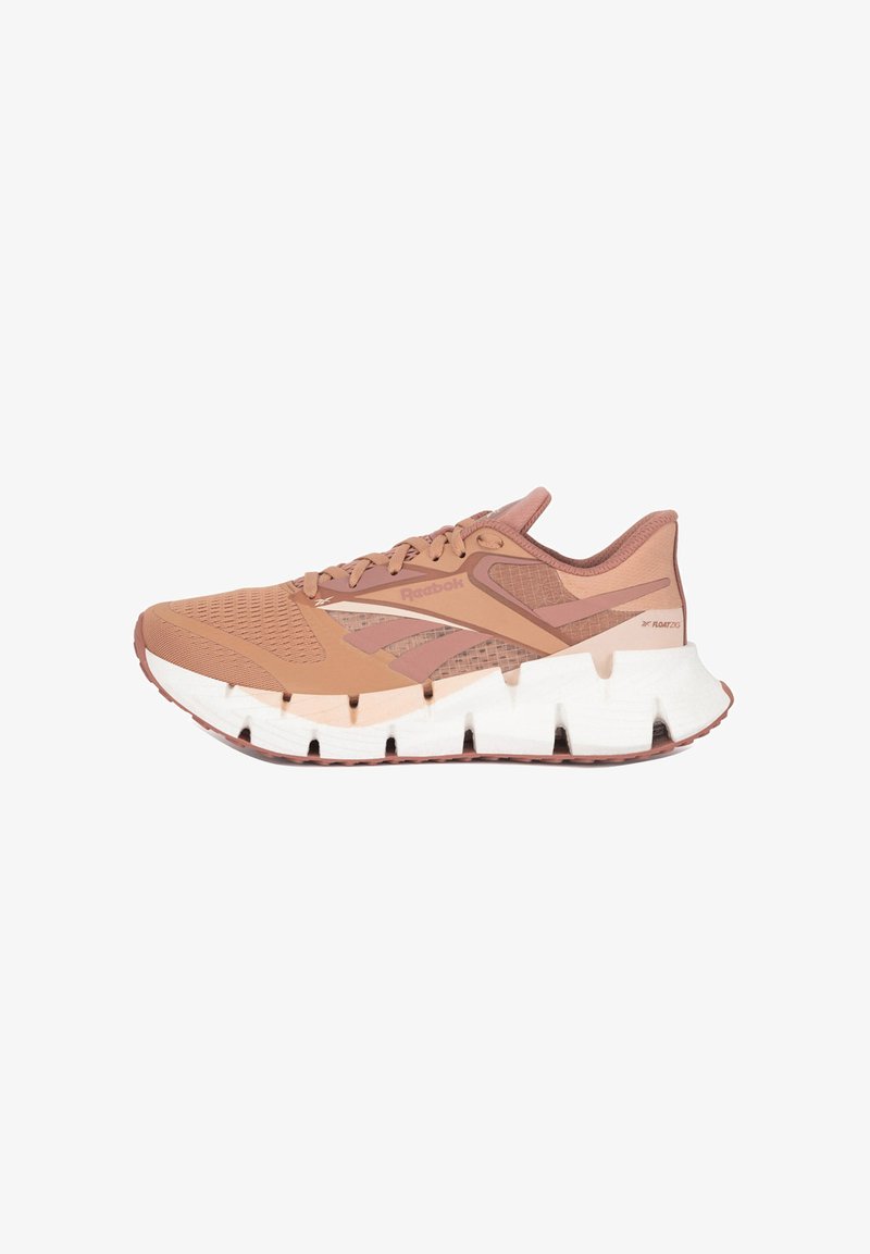 Bežecká obuv Reebok má svetlohnedý syntetický zvršok s sieťovanými akcentmi, hrubú bielu a hnedú podrážku a zaoblený dizajn päty pre podporu.