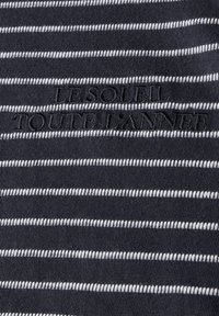 Námořnická modrá tkanina s vodorovnými bílými pruhy; obsahuje text "LE SOLEIL TOUTE L'ANNÉE" vyšitý černými písmeny. Hladká textura.