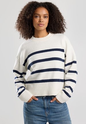 Maglione crema con righe orizzontali blu, colletto e polsini a coste, vestibilità rilassata, abbinato a jeans blu a vita alta.