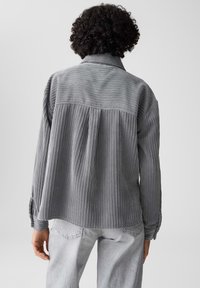 Grijze corduroy overhemd met verticale ribbelstructuur, knoopmanchetten en een relaxte pasvorm. Heeft een schouderpasontwerp over de rug.