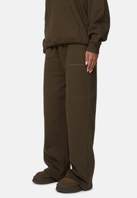 Hoodie surdimensionné vert olive foncé avec poche kangourou et pantalon de survêtement large assorti arborant un logo sur la cuisse. Texture douce.