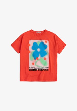T-shirt rossa a maniche corte con una grande grafica di un fiore blu e foglie verdi, puntini arancioni e testo "OGNI ESTATE HA UNA STORIA BOBO CHOSES."