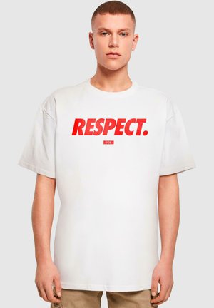 T-shirt oversize blanc avec un texte rouge en gras qui dit "RESPECT." et un petit logo en dessous. Manches courtes et col rond.