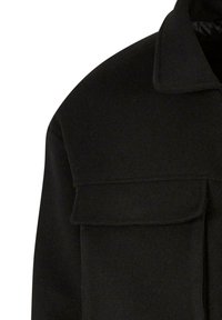 Veste en laine noire avec une grande poche à rabat sur la poitrine et un large col, vue de la partie supérieure du torse.