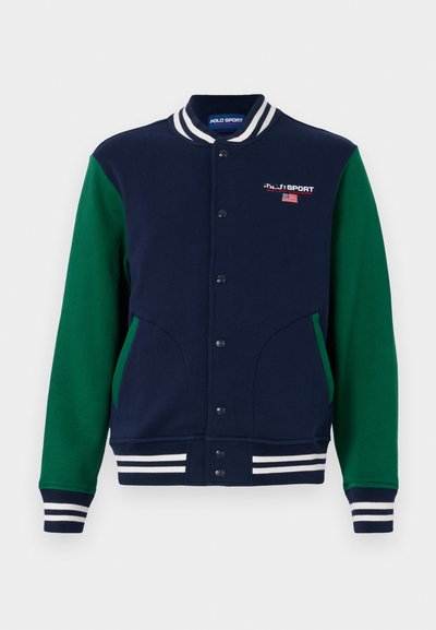 Ναυτικό μπλε varsity jacket με πράσινα μανίκια, λευκή ριγέ λαιμόκοψη και μανσέτες. Διαθέτει κουμπιά με σύστημα snap και δύο πλαϊνές τσέπες. Εμφανίζεται το λογότυπο "Polo Sport".