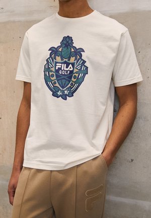 Biała bawełniana koszulka z kolorowym, szczegółowym nadrukiem z palmami i napisem "Fila Golf" na środku, noszona z beżowymi spodniami.