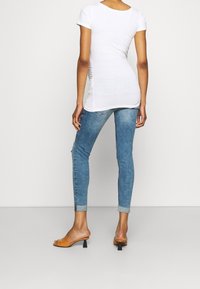 Camiseta blanca ajustada de manga corta, con los laterales fruncidos. Combinada con jeans skinny azules, doblados en los tobillos, y sandalias de tacón color tostado.