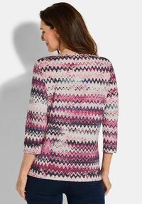 Gemusterte Bluse mit drei Viertelärmeln, die ein gewelltes Design in Pink-, Weiß- und Marineblau-Tönen aufweist und aus einem weichen Stoff gefertigt ist.