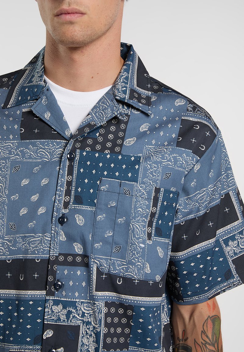 Camicia a maniche corte con design patchwork in blu e nero, con motivi paisley e geometrici; realizzata in tessuto leggero.